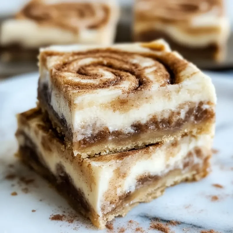 Stack of ooey-gooey cinnamon roll cheesecake bars with visible cinnamon swirls and creamy layers on a marble surface