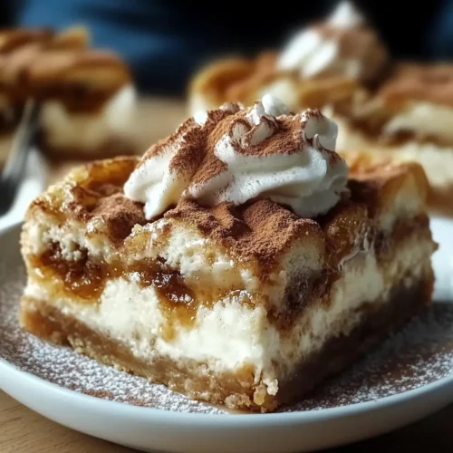 Close-up of ooey-gooey cinnamon roll cheesecake bars topped with whipped cream and dusted with cocoa powder