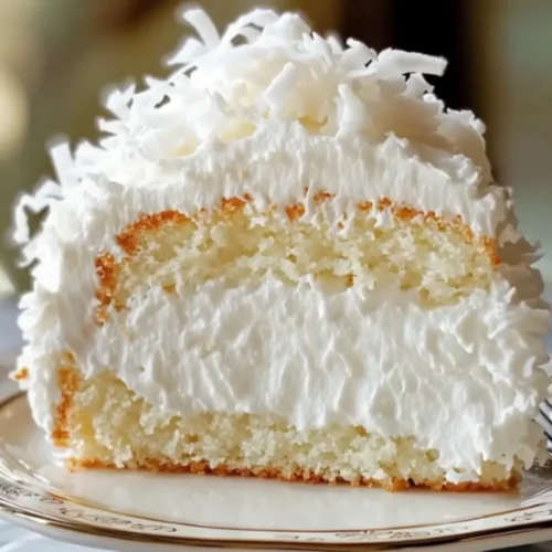 Slice of Coconut Cloud Cake with fluffy white coconut frosting and moist vanilla cake layers