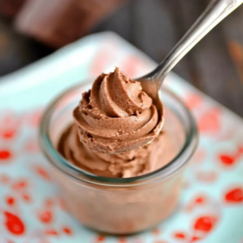 Spoonful of Easy Chocolate Mousse lifted from a glass jar, showing smooth and creamy texture.