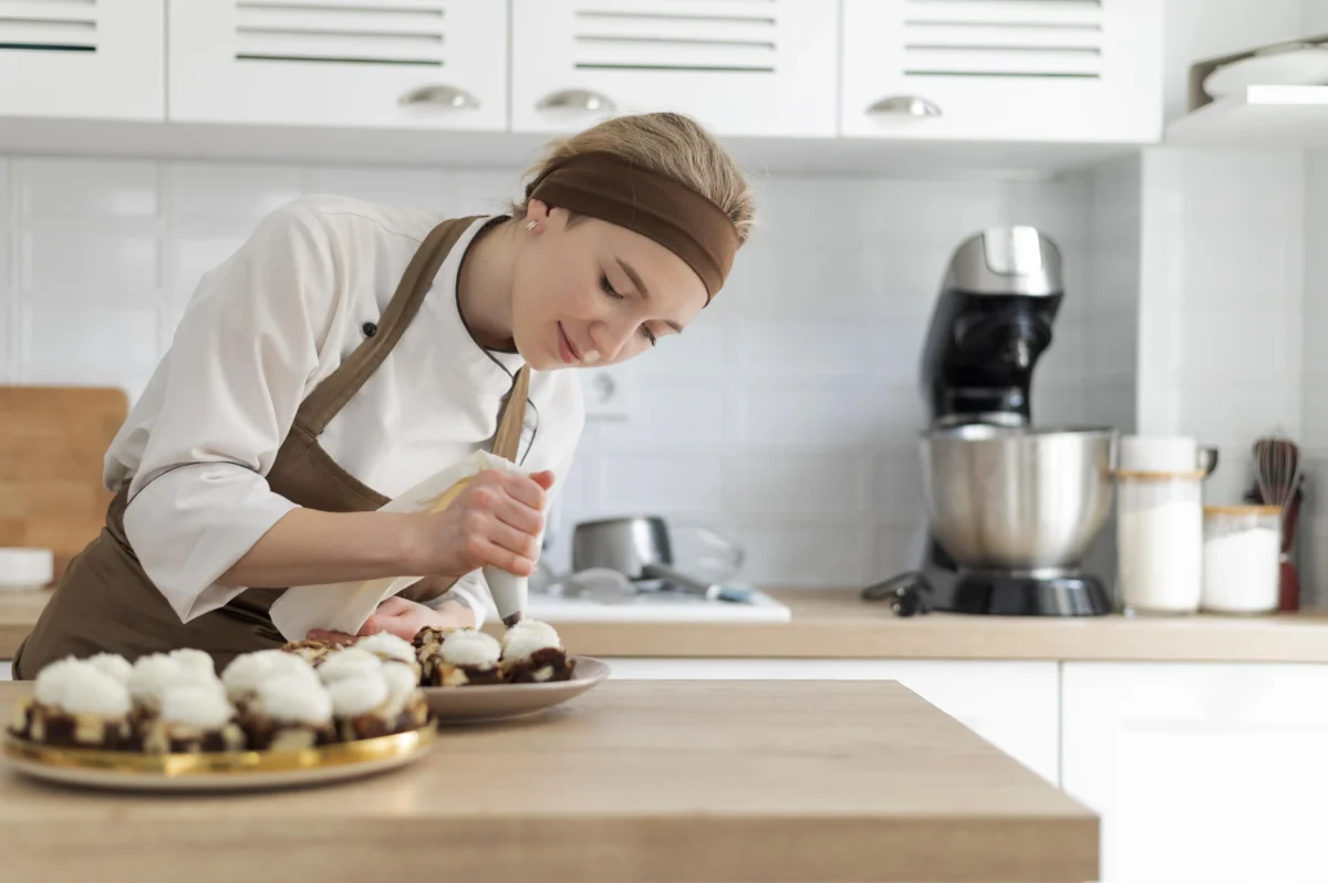 Female pastry chef decorating desserts with cream in a modern kitchen 