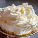 A fork taking a swirl of rich, creamy 300 Dollar Frosting Recipe from a dessert in a silver bowl.