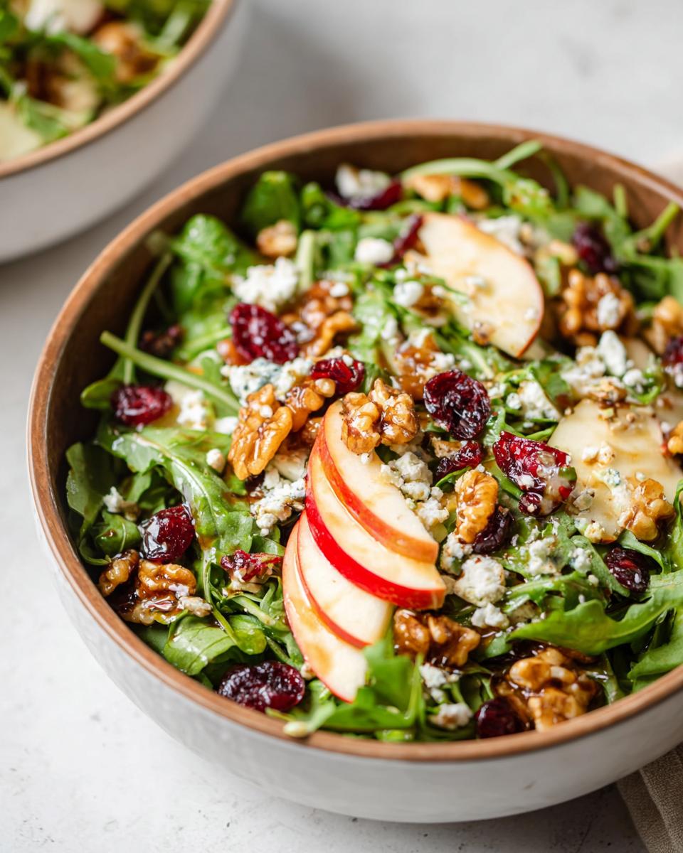 A vibrant Apple Walnut Salad in a wooden bowl, featuring crisp apple slices, crunchy walnuts, dried cranberries, and crumbled blue cheese over a bed of greens.