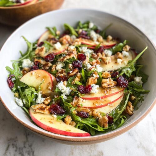 A refreshing Apple Walnut Salad featuring crisp apple slices, crunchy walnuts, dried cranberries, and crumbled blue cheese on a bed of arugula.