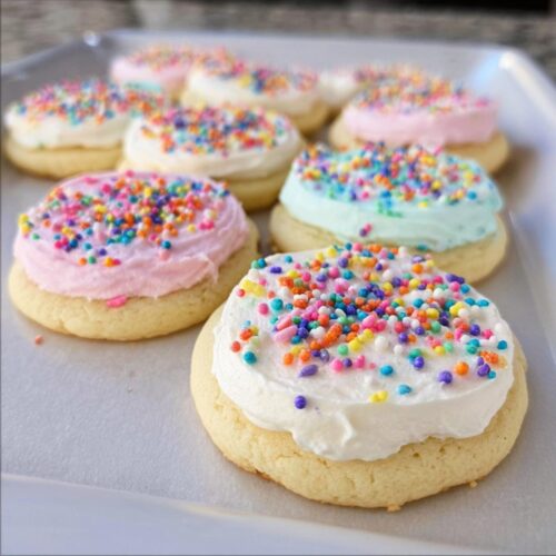 Close-up of sugar cookies topped with The Best Sugar Cookie Frosting in various pastel colors and rainbow sprinkles.