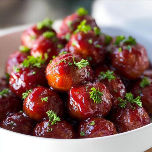 A bowl overflowing with glistening Christmas Cranberry Meatballs, garnished with fresh parsley.