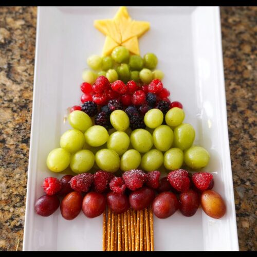 A beautiful Christmas Tree Fruit Platter made with green grapes, red berries, blackberries, and a cheese star.