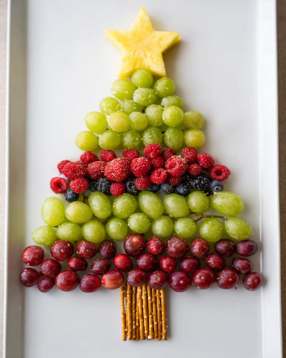A festive Christmas Tree Fruit Platter made with green grapes, red grapes, raspberries, blueberries, and a pineapple star.