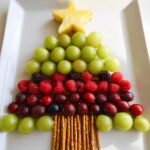 A visually appealing Christmas Tree Fruit Platter made with green grapes, raspberries, blackberries, and cherries, topped with a pineapple star.