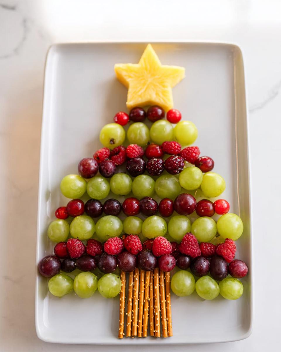 A festive Christmas Tree Fruit Platter made with green and red grapes, raspberries, blackberries, and a starfruit topper.