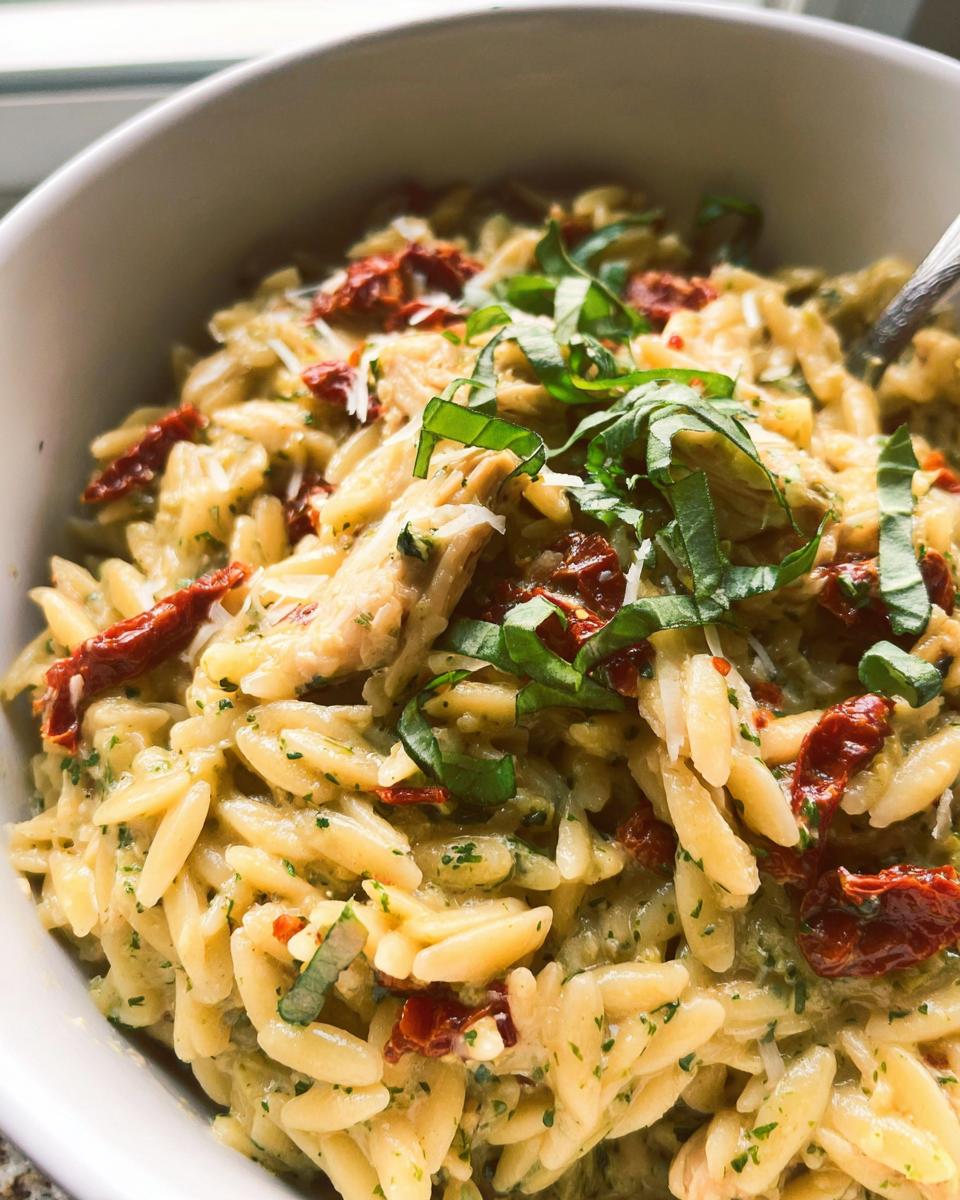 A close-up of Creamy Pesto Orzo with Sun-Dried Tomatoes, garnished with fresh basil and grated cheese.