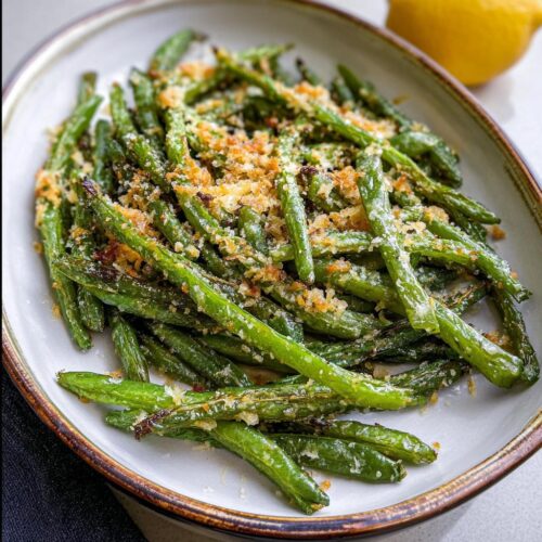Close-up of a serving dish filled with Crispy Garlic Parmesan Roasted Green Beans, topped with breadcrumbs and cheese.