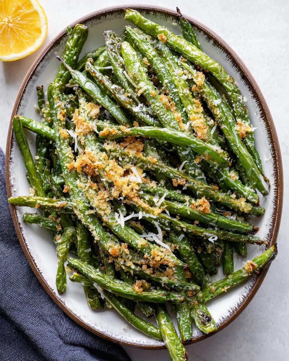 A close-up overhead view of a bowl filled with Crispy Garlic Parmesan Roasted Green Beans, topped with grated cheese and breadcrumbs.