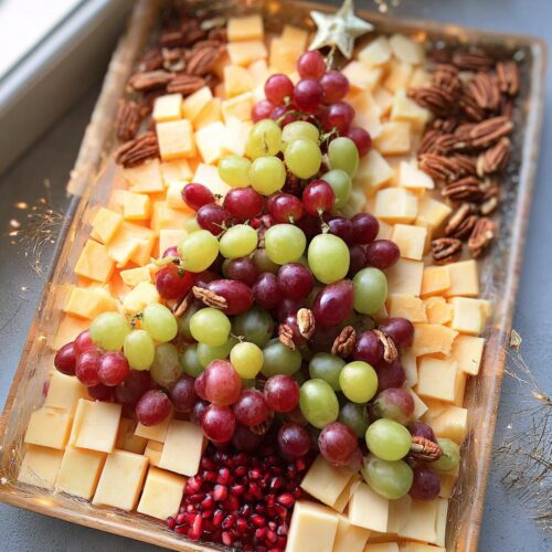 A festive Fruit and Cheese Christmas Board arranged in the shape of a Christmas tree, featuring grapes, cheese cubes, pecans, and pomegranate seeds.