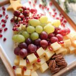 A festive Fruit and Cheese Christmas Board arranged in the shape of a tree, featuring grapes, pomegranate seeds, cheese cubes, and pecans.