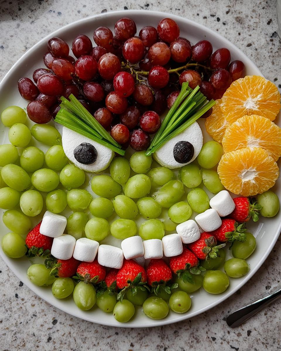 A festive Grinch Fruit Tray made with green and red grapes, marshmallows, strawberries, and orange slices.