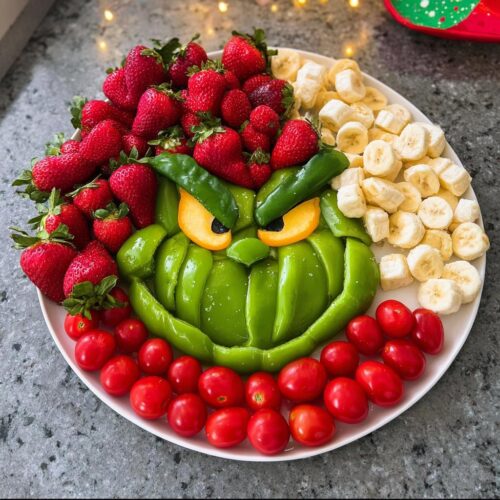 A Grinch Fruit and Veggie Tray made with green bell peppers, strawberries, bananas, and tomatoes.
