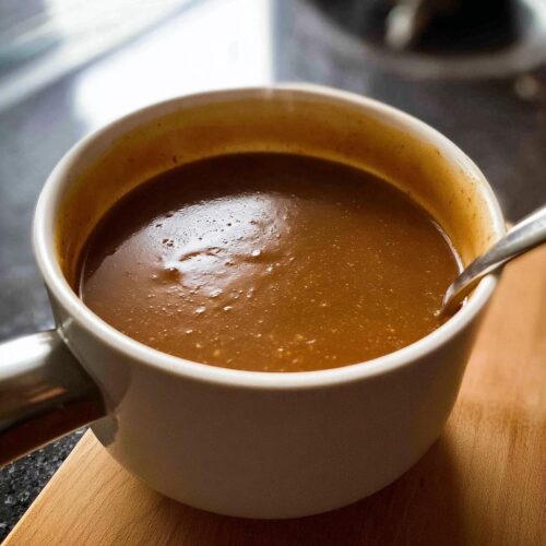 A close-up shot of rich, smooth Homemade Gravy in a white pot with a spoon.