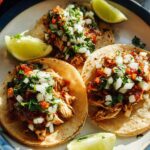 Three delicious Instant Pot Lemon Garlic Chicken Tacos topped with salsa, onions, and cilantro, served with lime wedges.