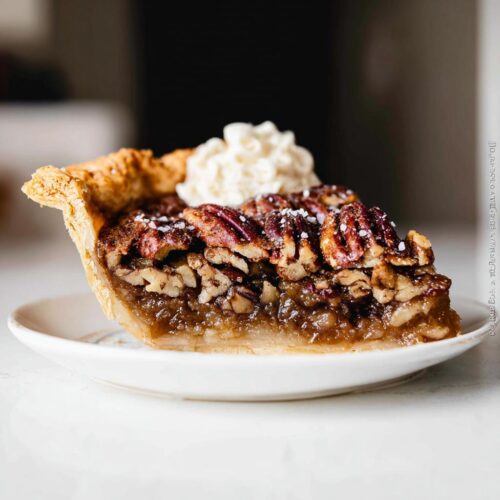 A delicious slice of maple pecan pie topped with whipped cream and a sprinkle of sea salt.