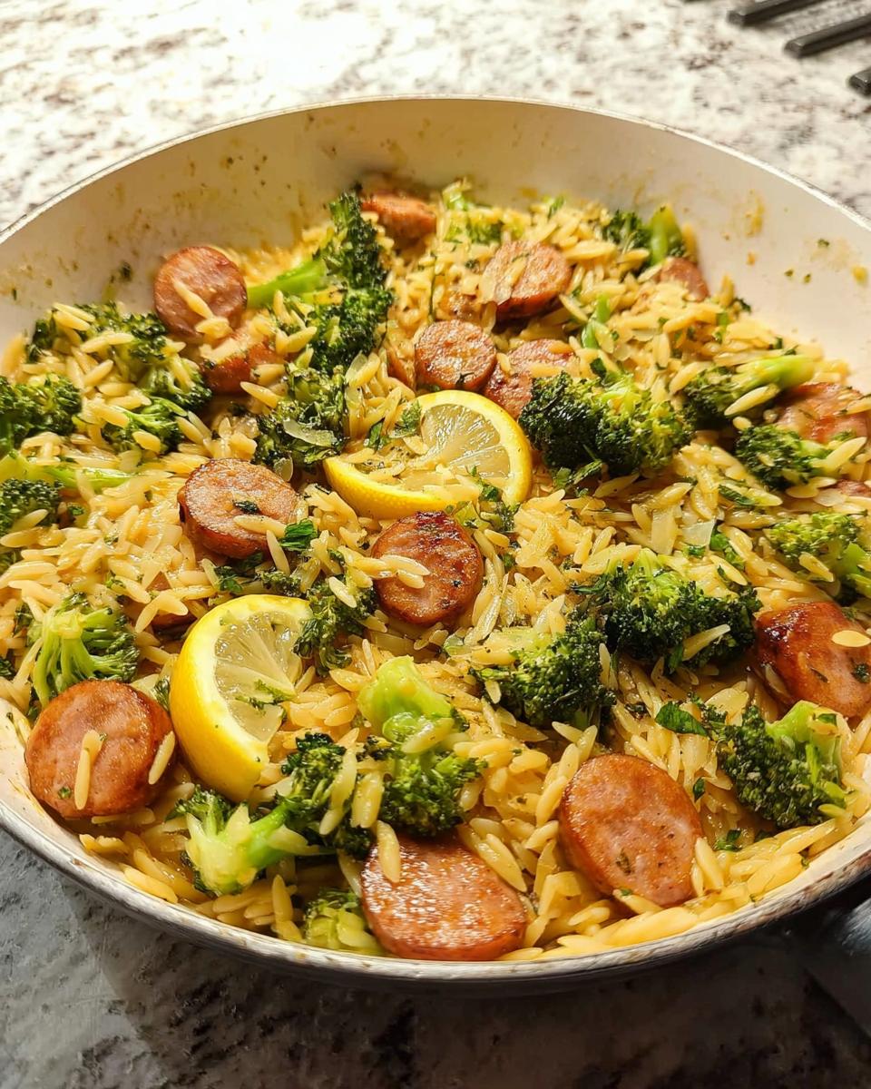 Close-up of a one-pan lemon garlic orzo with sausage and broccoli, garnished with lemon slices.