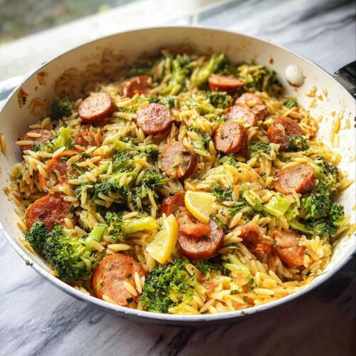 A close-up of a one-pan lemon garlic orzo with sausage and broccoli, garnished with lemon wedges.