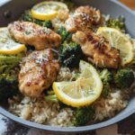 A close-up of a one-pot lemon chicken rice with broccoli dish, featuring golden-brown chicken pieces, vibrant broccoli florets, and fluffy rice, garnished with lemon slices and parsley.