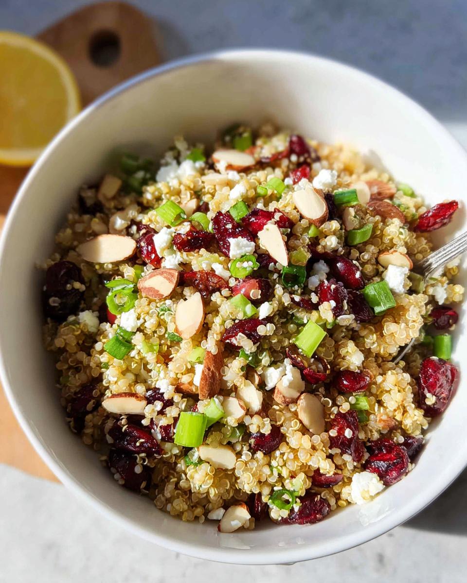 A close-up of a Quinoa Cranberry Bowl topped with feta cheese, sliced almonds, and green onions.