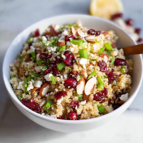 A close-up of a Quinoa Cranberry Bowl filled with fluffy quinoa, dried cranberries, crumbled feta cheese, sliced almonds, and chopped green onions.