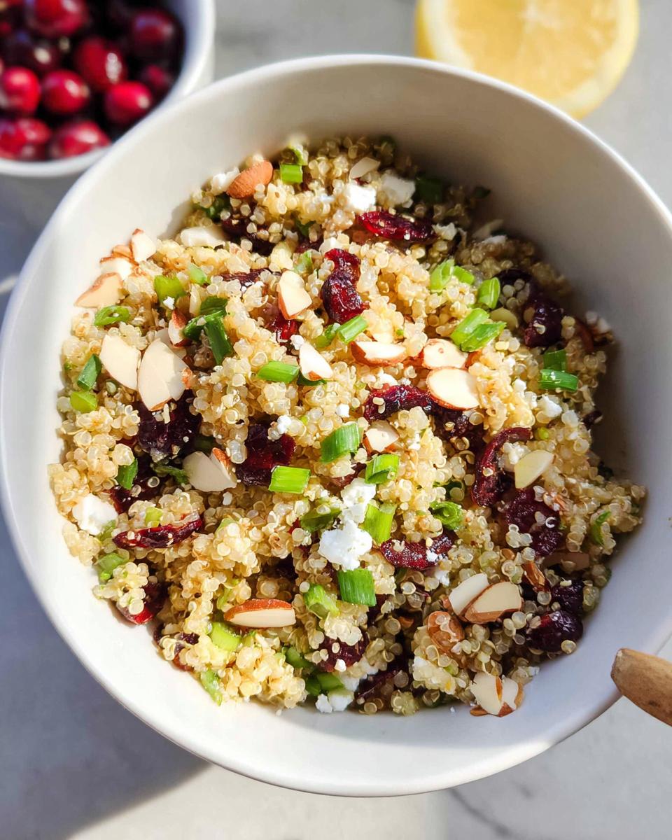 A close-up of a Quinoa Cranberry Bowl topped with sliced almonds, crumbled feta cheese, and chopped green onions.