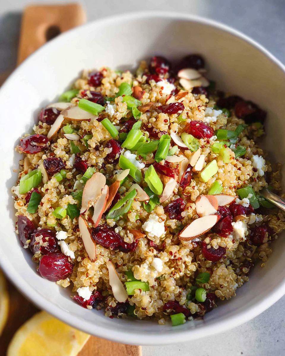 A close-up of a Quinoa Cranberry Bowl, featuring fluffy quinoa, dried cranberries, crumbled feta, sliced almonds, and chopped green onions.