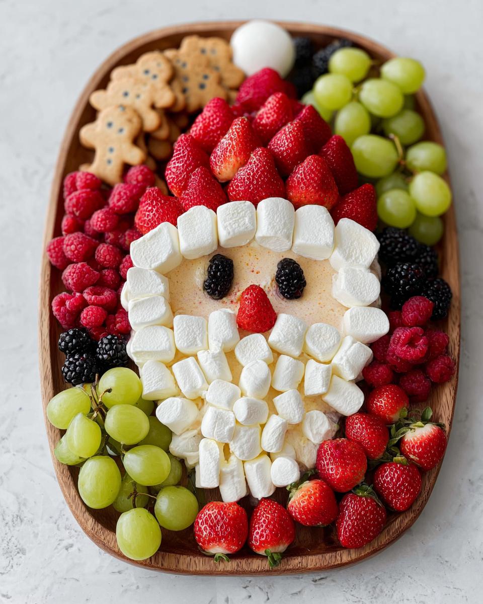 A festive Santa Fruit Tray made with strawberries, marshmallows, grapes, raspberries, blackberries, and gingerbread cookies.