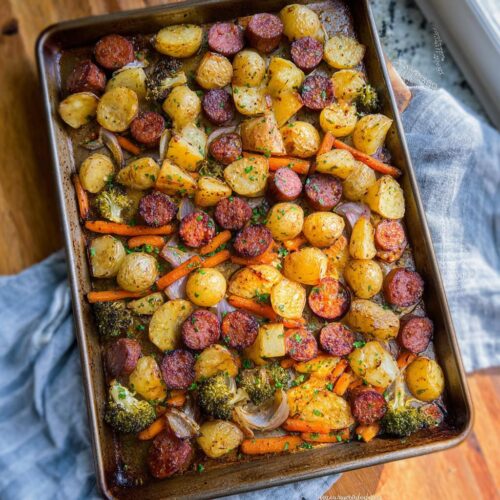 A full sheet pan of Sheet Pan Ranch Potatoes & Sausage, with roasted potatoes, sausage, carrots, broccoli, and onions.