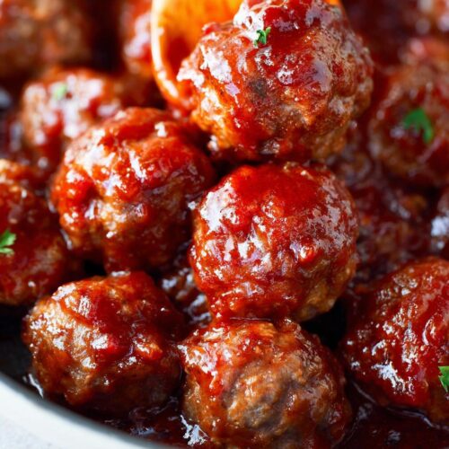 Close-up of juicy Spicy Cranberry Cocktail Meatballs coated in a rich, glossy sauce, with a wooden spoon lifting one.