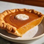 A delicious slice of sweet potato pie with a dollop of whipped cream and a sprinkle of cinnamon.