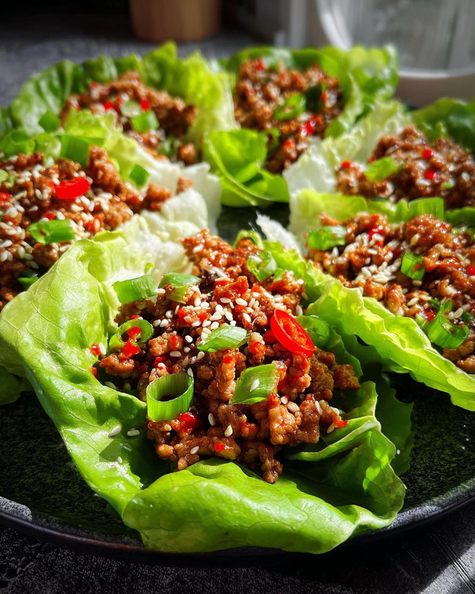 Close-up of fresh Turkey Lettuce Wraps filled with seasoned ground turkey, topped with sesame seeds, chili, and green onions.
