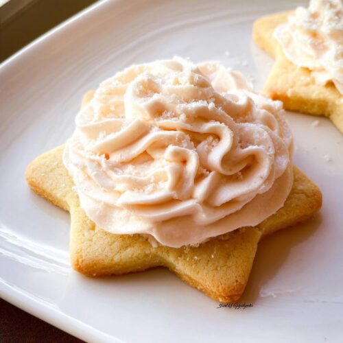 A star-shaped sugar cookie topped with a swirl of fluffy whipped sugar cookie frosting, resembling a rose.