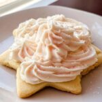 A star-shaped sugar cookie topped with fluffy, piped whipped sugar cookie frosting and sprinkled with sugar.