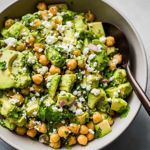 A close-up overhead view of a vibrant Avocado Chickpea Bowl topped with crumbled white cheese and fresh cilantro.