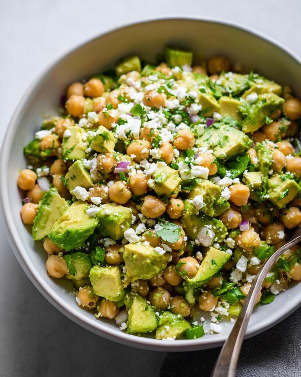 Close-up view of a vibrant Avocado Chickpea Bowl topped with crumbled white cheese and fresh herbs.