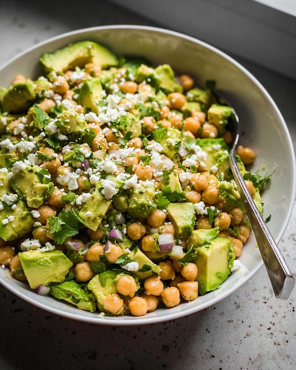 A close-up of a vibrant Avocado Chickpea Bowl featuring diced avocado, chickpeas, feta cheese, and cilantro.