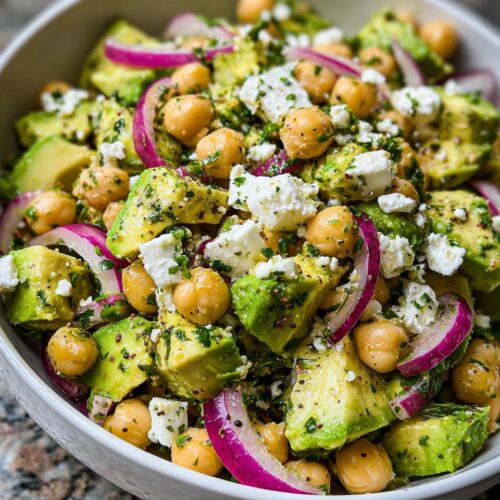 A vibrant close-up of Chickpea Feta Avocado Salad featuring chunks of avocado, chickpeas, feta cheese, and red onion slices.