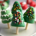 Close-up of festive Christmas Tree Cake Pops decorated with green frosting and colorful sprinkles, on a white plate.