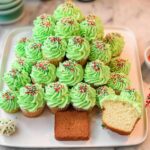 A Christmas Tree Cupcake Platter made with green frosted cupcakes and festive sprinkles, with one cupcake cut open.