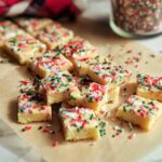 Close-up of cut Confetti Holiday Shortbread slices topped with colorful festive sprinkles on parchment paper.