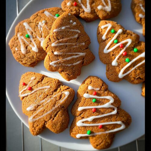 A plate of perfectly crispy gingerbread cookies decorated with white icing and festive red and green sprinkles.