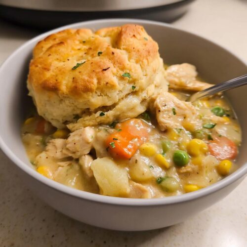 A close-up of Crockpot Chicken Pot Pie with Potatoes topped with a golden biscuit in a white bowl.