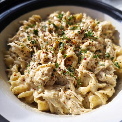 Close-up of creamy Crockpot Garlic Parmesan Chicken Pasta topped with parsley and red pepper flakes.