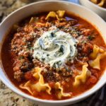 Close-up of a bowl of hearty Crockpot Lasagna Soup with ground meat, pasta, and a swirl of herbed ricotta cheese.