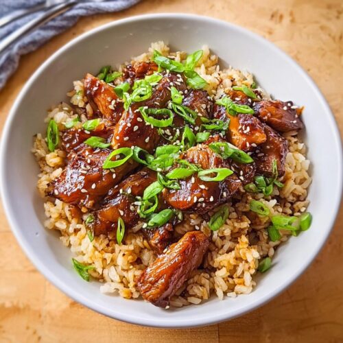 A white bowl filled with Crockpot Teriyaki Chicken with Rice, topped with sesame seeds and green onions.